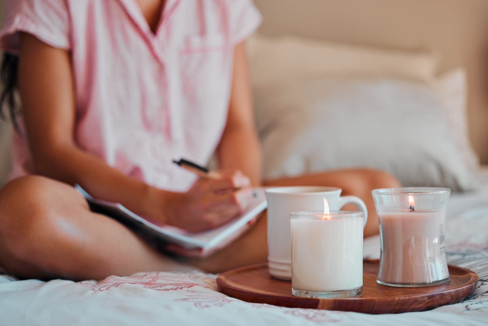 A woman journaling in bed with a mug and candles